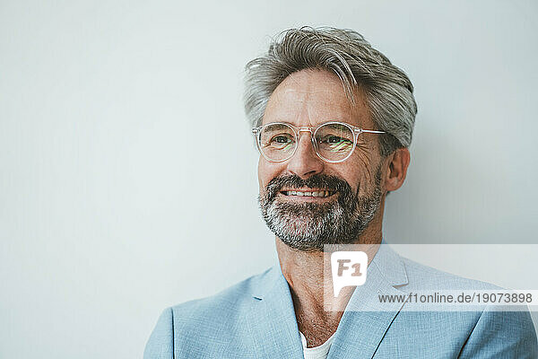Smiling businessman wearing eyeglasses in front of white wall