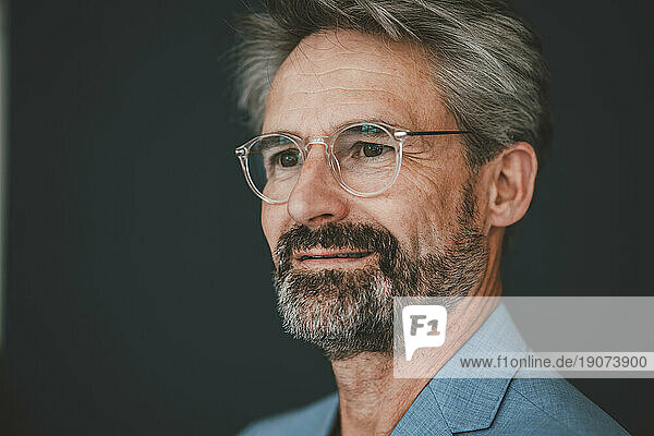 Contemplative businessman wearing eyeglasses against teal background