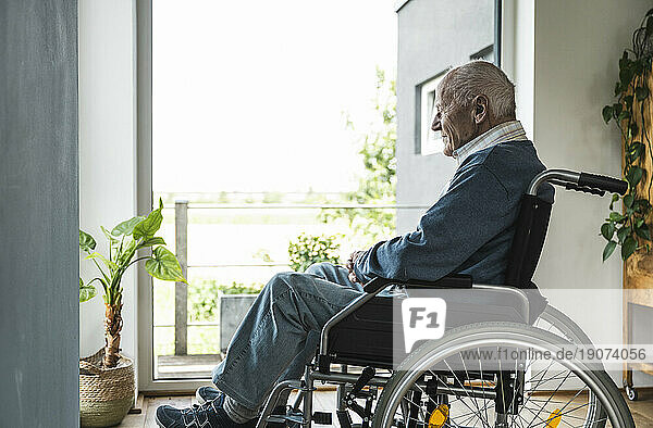 Senior man sitting in wheelchair by window at home