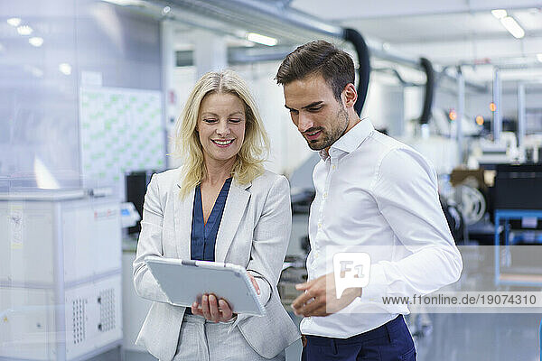 Smiling blond businesswoman discussing over digital tablet with male colleague at factory