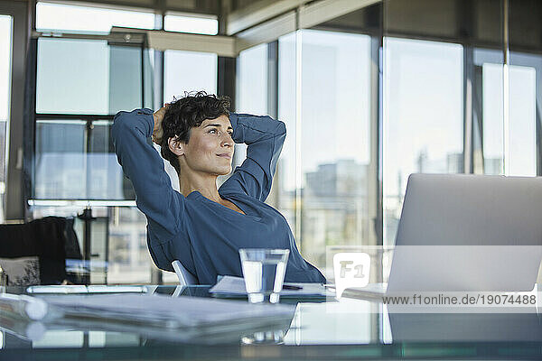 Smiling businesswoman sitting at desk in office with laptop having a break