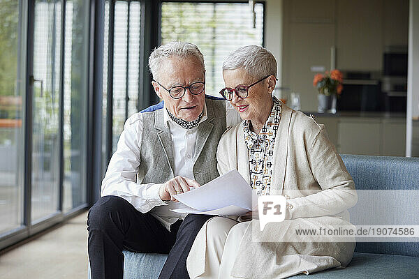 Senior couple sitting on couch at home reading document
