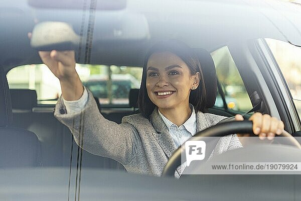 Lächelnde Geschäftsfrau beim Einstellen des Rückspiegels ihres Autos