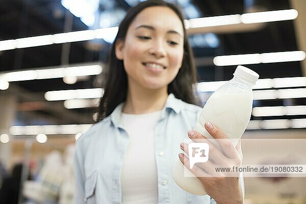 Fröhliche asiatische Frau hält Flasche Milch Supermarkt
