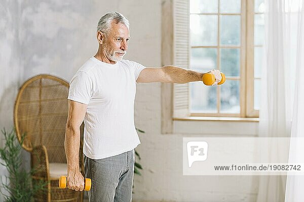 Fitter älterer Mann  der mit orangefarbenen Hanteln zu Hause trainiert
