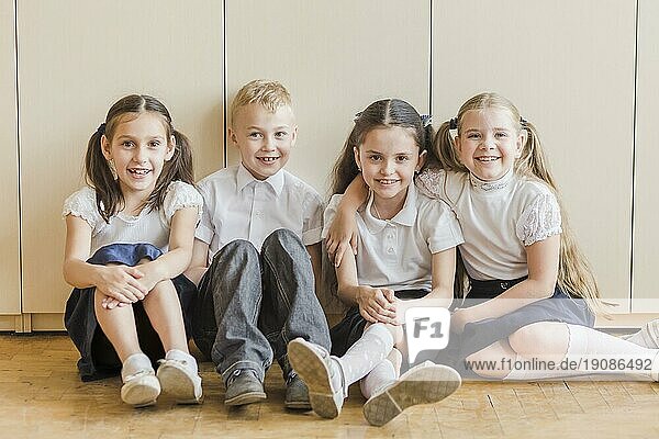 Fröhliche Kinder sitzen auf dem Boden der Schule