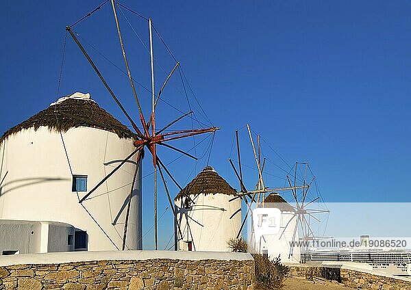 Berühmte Touristenattraktion von Mykonos  Kykladen  Griechenland. Drei traditionelle  weiß getünchte Windmühlen am Wasser. Sommer  blauer Himmel  Kreuzfahrtschiff beim Verlassen des Hafens im Hintergrund. Reiseziel  ikonische Ansicht