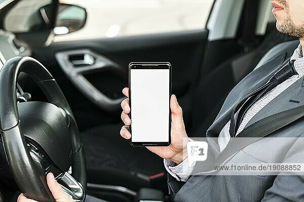 Nahaufnahme eines Geschäftsmannes  der Auto fährt und ein Mobiltelefon mit weißem Bildschirm zeigt