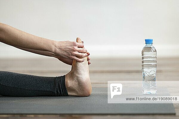 Seitenansicht Frau Stretching Yogamatte mit Wasserflasche