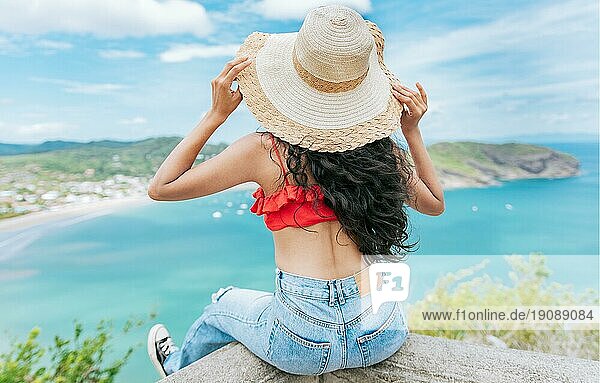 Rückansicht Tourist Mädchen sitzt an einem Aussichtspunkt mit Blick auf den Strand. Rückenansicht der Frau im Urlaub Blick auf den Strand an einem Aussichtspunkt