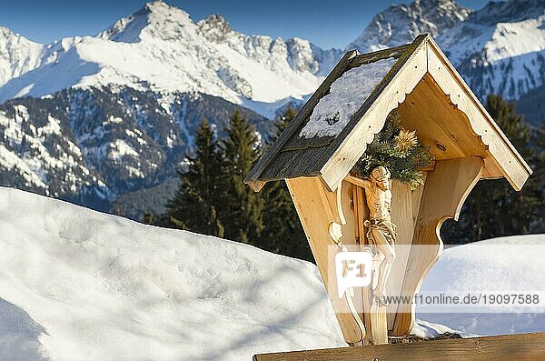 Eine Holzskulptur des gekreuzigten Jesus Christus vor dem Hintergrund der Alpen im Winter. Blick auf die Berge. Religion und Kultur. Österreich