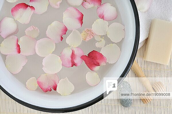 Schüssel mit Wasser und Rosenblütenblättern neben Massageroller Seife und Handtuch