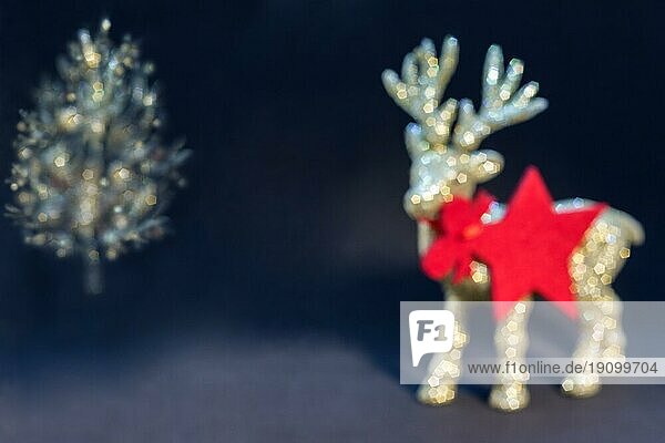 Bokeh Weihnachtshintergrund. Goldene  glänzende Rentierfigur mit einem Weihnachtsbaum auf einem dunklen Hintergrund. Weihnachtskarte  Geschenkkarte  roter Stern  Anhänger. Weihnachtstapete mit Kopierraum