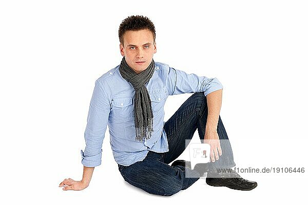Lässiger attraktiver junger Mann auf dem Boden sitzend  vor weißem Hintergrund