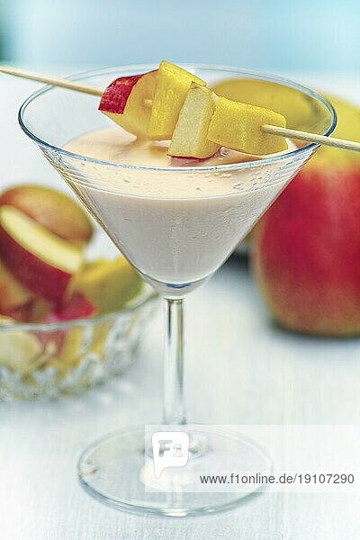 Ein Glas mit Mango Birne Shake. Diagonal über dem Glas liegen mehrere Fruchtstücke  die auf einen Stab aufgespießt sind. Der Unter- Hintergrund ist bewußt unscharf gehalten