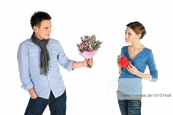 Junges attraktives Paar in Liebe. Frau gibt ihr Herz  Mann bietet Blumen  vor weißem Hintergrund