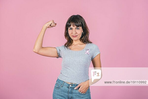 Eine Frau trägt ein rosa Brustkrebs Band und zeigt ihre Armmuskeln. Sieg über Brustkrebs