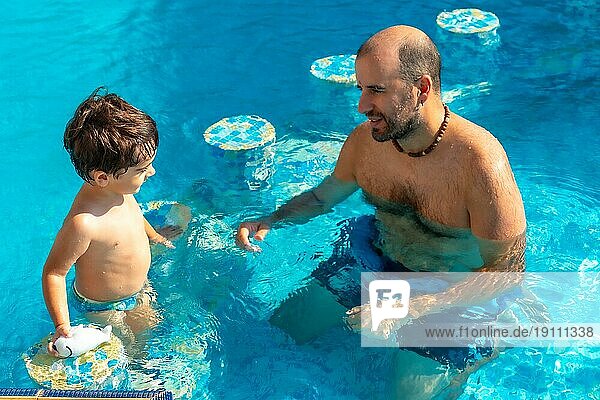 Vater und Sohn im Pool im Sommer spielen genießen und lächelnd im Urlaub