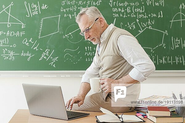Senior Professor sitzt am Schreibtisch und tippt auf einem Laptop