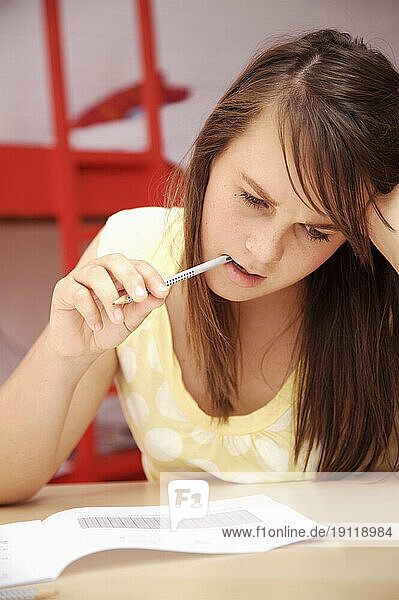 Young girl studying with pencil in mouth