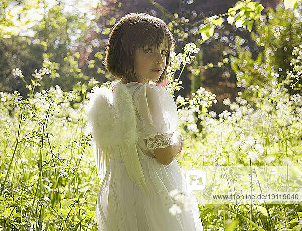 Portrait of young girl in a white fairy costume standing in a garden