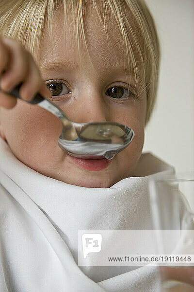 Close up of young blonde boy drinking water with a spoon