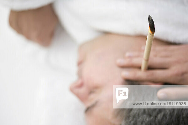 Close up of man's head with burning ear candle
