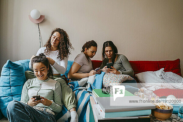 Fröhliche Freundinnen benutzen Smartphones im heimischen Wohnzimmer