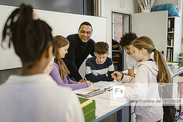 Happy teacher with multiracial students at desk in classroom