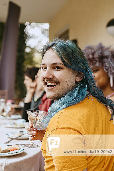 Porträt eines fröhlichen schwulen Mannes mit gefärbten Haaren  der sich mit Freunden bei einer Dinnerparty im Hinterhof vergnügt