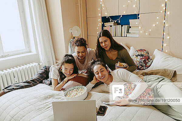 Cheerful multiracial friends watching movie together on laptop at home