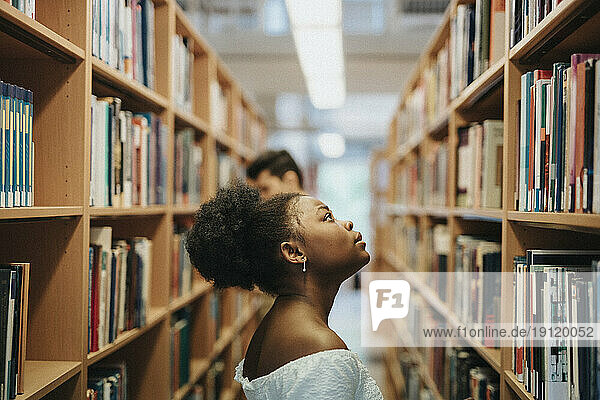 Side view of student searching books on bookshelf in library at university