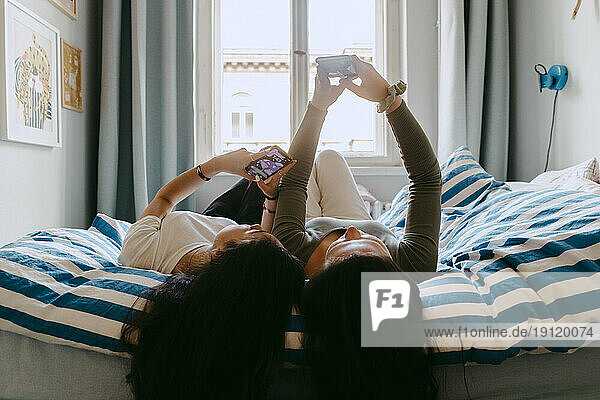 Freundinnen benutzen ihr Smartphone  während sie zu Hause im Bett liegen