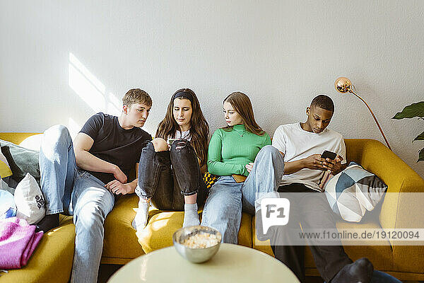 Junge multirassische Freunde benutzen Smartphones  während sie zu Hause auf dem Sofa sitzen
