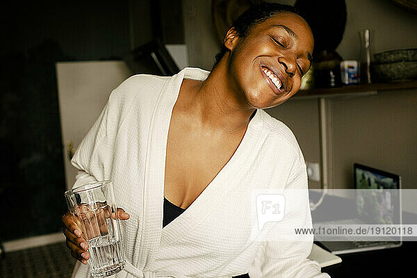 Fröhliche junge Frau hält ein Trinkglas in der Hand und tanzt in der Küche zu Hause