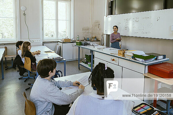Lächelnde Lehrerin unterrichtet Schüler am Schreibtisch sitzend im Klassenzimmer