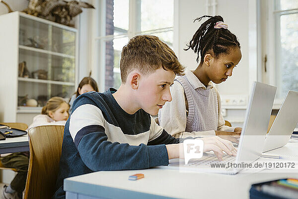 Konzentrierter Schüler  der mit seiner Freundin am Schreibtisch im Klassenzimmer einen Laptop benutzt