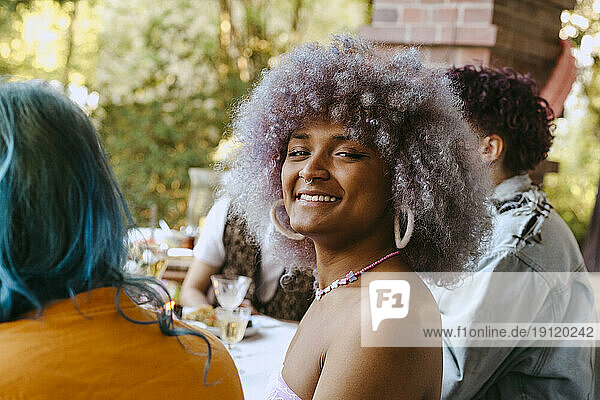 Seitenansicht Porträt einer lächelnden Transfrau mit lockigem Haar während einer Dinnerparty im Hinterhof