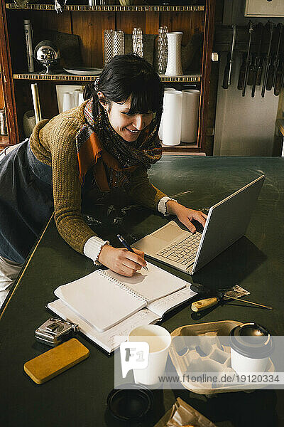 Lächelnde Unternehmerin arbeitet an einem Laptop in einem Upcycling-Laden
