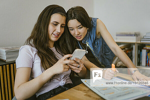 Junge Freundinnen teilen sich ein Smartphone  während sie zu Hause zusammen lernen