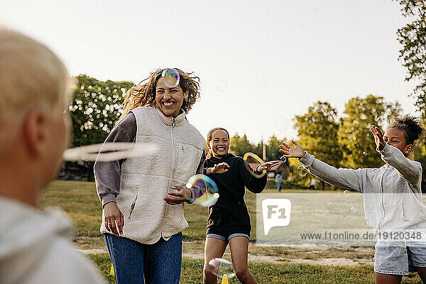 Fröhliche Kinder spielen inmitten von Seifenblasen mit einem Betreuer auf dem Spielplatz eines Ferienlagers