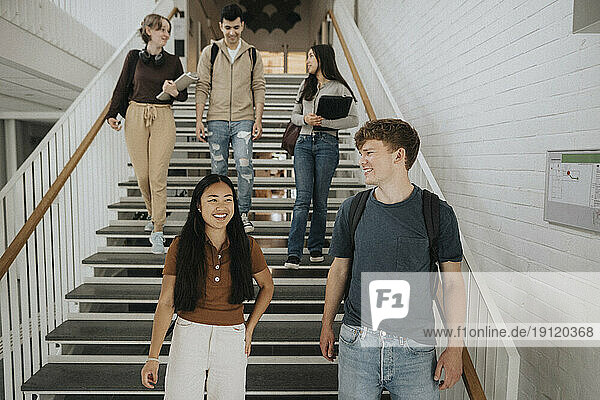 Happy multiracial students talking while moving down on steps in university