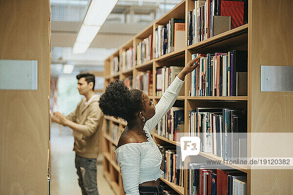 Seitenansicht eines Studenten  der in der Bibliothek der Universität Bücher im Regal sucht