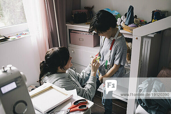 Mother using tape measure while sewing clothes for son at home