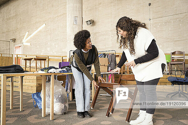 Female workers discussing over wooden chair at recycling center