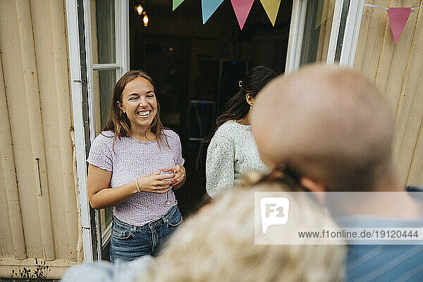 Happy woman holding wineglass while enjoying with friends during dinner party at cafe