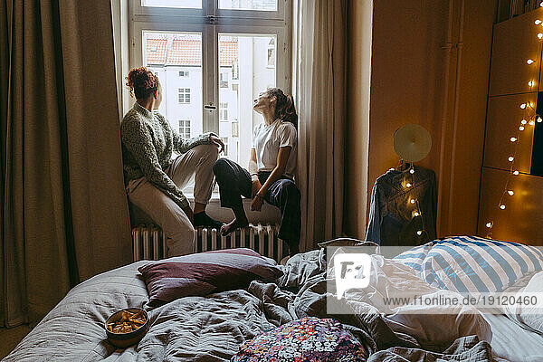 Young female friends sitting at window in bedroom