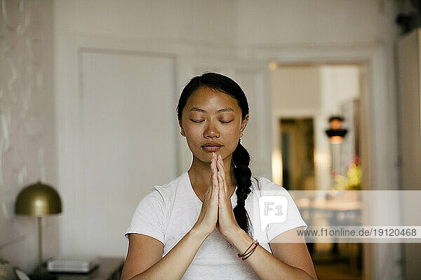 Junge Frau mit gefalteten Händen beim Meditieren zu Hause