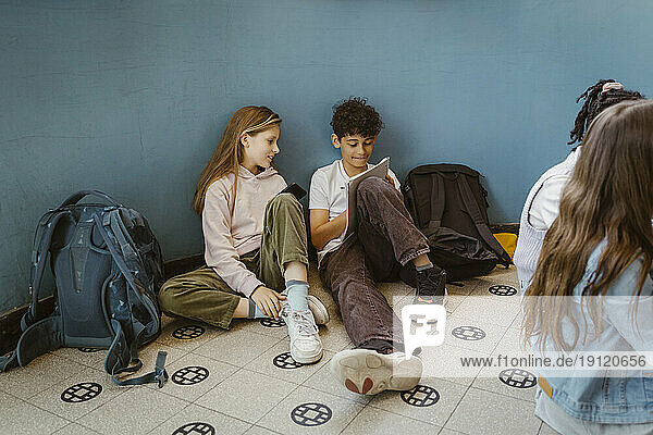 Junge und Mädchen lernen zusammen  während sie in der Nähe der Wand im Schulgebäude sitzen
