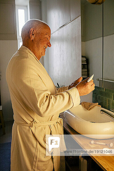 Älterer Mann lächelnd beim Auftragen von Feuchtigkeitscreme im Badezimmer zu Hause